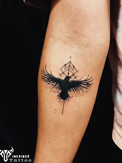A blackwork crow tattoo with a geometric background on the inner forearm. The abstract, splatter-ink style provides excellent coverage for old tattoos.