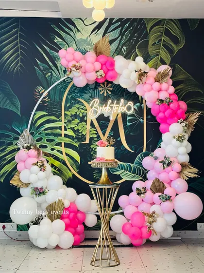 A vibrant "Bride to be" decoration against a tropical leaf wallpaper. The circular gold frame is adorned with a bright pink and white balloon garland, creating a fun and trendy look.