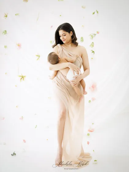 A full-length portrait of a mother cradling her newborn. The image has a graceful, almost sculptural quality, celebrating the beauty of motherhood.