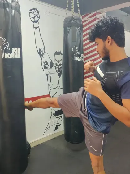 A student practices his kicking technique on the heavy bag, an essential drill for developing power and precision in Muay Thai and kickboxing.
