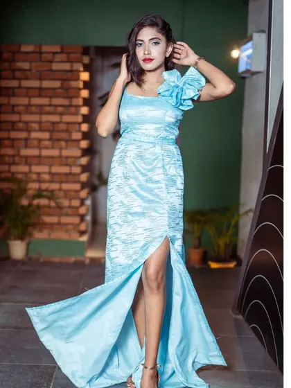 A model looking fabulous in a light blue satin gown with a high slit and a floral shoulder detail. This is a great rental option for a party or event.