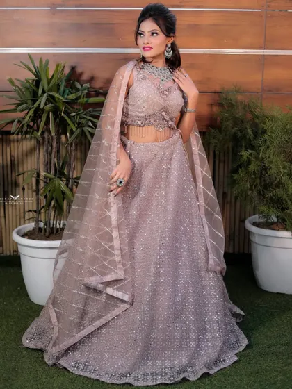 A full-length portrait of a bride in a shimmering lavender lehenga, perfect for a reception or sangeet. The outdoor setting with potted plants adds a fresh, modern vibe.