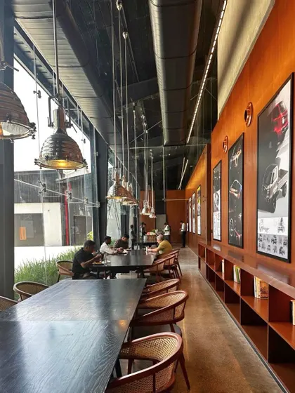 The cafeteria in the Automobile Design Studio is a long, light-filled space with views of the campus. Industrial pendant lights and simple, robust furniture create a functional and social hub for employees.