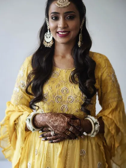 A beautiful client looking radiant at her haldi ceremony, with her henna stain perfectly complementing her yellow outfit.