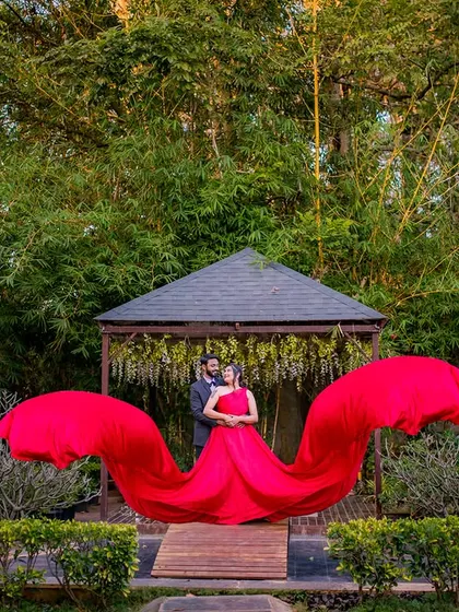 A wider angle of the popular "wing" pose. The flowing red gown creates a dramatic shape against the lush green bamboo background, making the couple stand out.