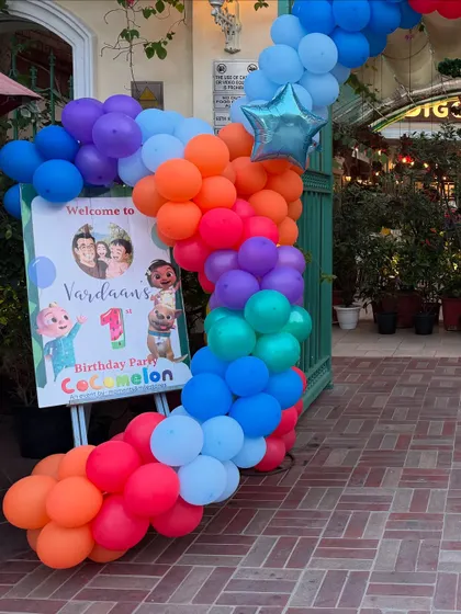 A vibrant, rainbow-colored balloon garland marks the entrance to Vardaan's Cocomelon-themed first birthday party.