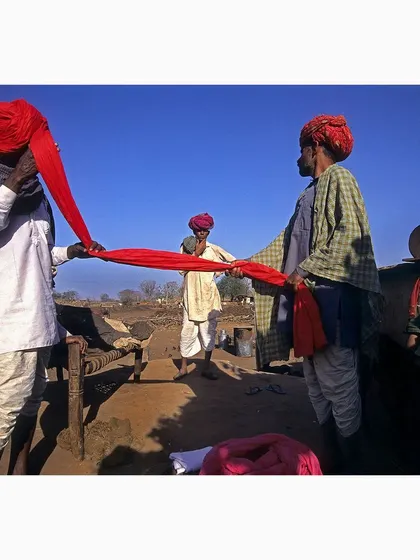 Men of the Gadaria tribe in Rajasthan meticulously tying a traditional red turban. This photograph documents a cultural practice, focusing on the vibrant color of the cloth and the collaborative nature of the act.