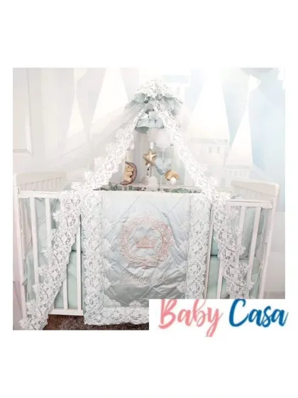 An ethereal and elegant bedding set in a soft mint green. The design is elevated by intricate white lace trim on the quilt, bumpers, and a beautiful canopy.