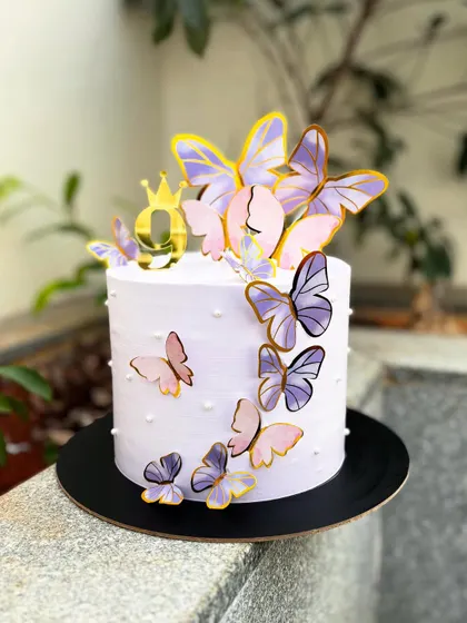 A delicate butterfly theme cake in a lovely lavender shade. The cake is adorned with cascading paper butterflies in shades of purple and pink.