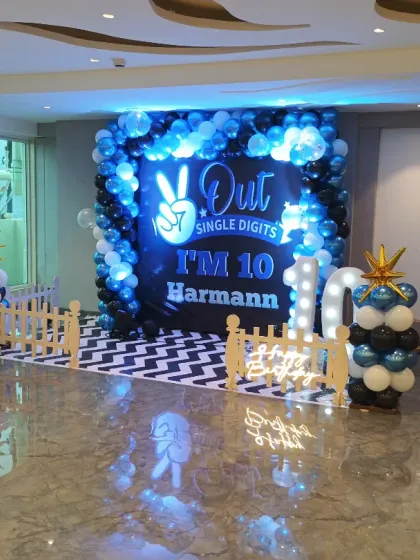 A stylish blue, black, and white balloon backdrop for a 10th birthday party. The setup includes marquee lights for the age and a custom floor print to complete the look.