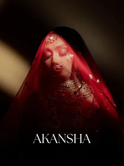 An artistic and moody bridal portrait. The bride's face is partially veiled in red, with her name "AKANSHA" elegantly written, creating a personalized and dramatic shot.