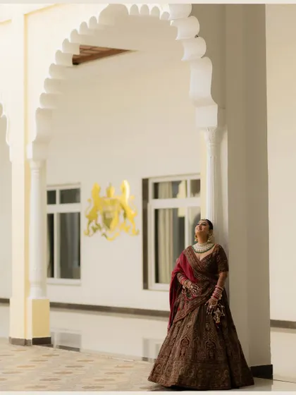 A wide shot of the bride looking up thoughtfully, framed by a grand white archway in a palace setting.