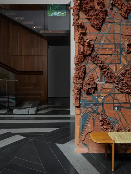 A terracotta wall mural by Pravat M, depicting an abstracted map, adds immense texture and narrative to this transitional space. The raw, earthy material contrasts with the polished, patterned granite flooring.