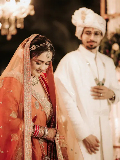 A quiet, contemplative moment during the wedding ceremony. The bride looks down with a gentle smile as the groom stands by her side, a beautiful, candid shot full of emotion.