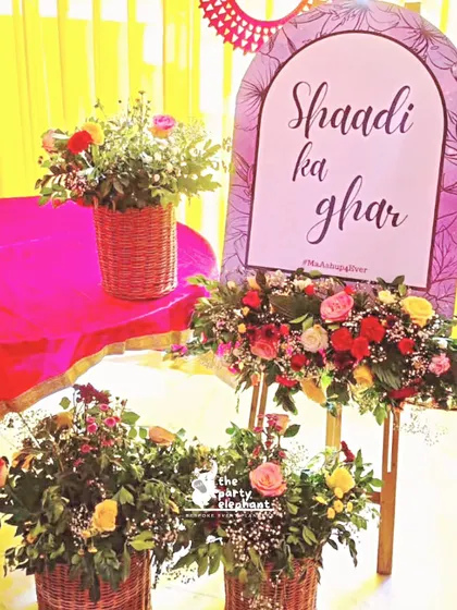 A custom 'Shaadi ka ghar' (Wedding House) sign, surrounded by beautiful floral arrangements, creating a warm and welcoming atmosphere for the wedding festivities.