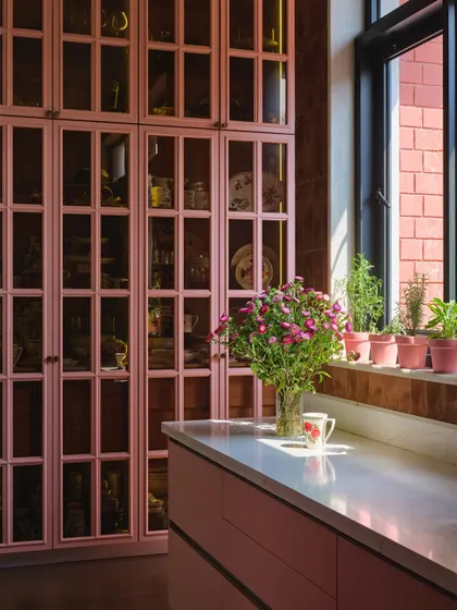 The rose-colored kitchen, with its clean lines and custom millwork, is both functional and beautiful. A window-side herb garden brings fresh ingredients and a touch of green into the space.