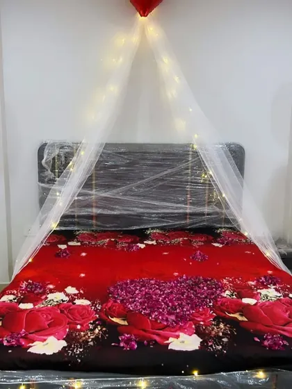 A close-up of the bed from the romantic room setup, showing the simple canopy created with fairy lights and a bedspread covered in rose petals.