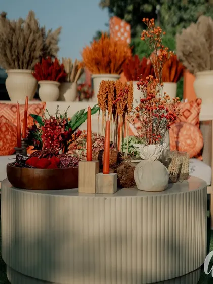 A detail shot of a lounge table centerpiece, featuring dried and fresh botanicals in shades of orange and red. The arrangement is both rustic and sophisticated, perfectly matching the event's theme.