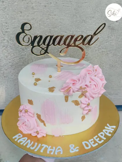 A simple and sweet pink and white engagement cake. The textured buttercream is accented with gold flecks and piped pink rosettes, topped with an elegant "Engaged" acrylic topper.