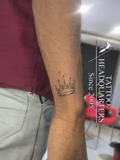 A small, simple crown outline tattoo on the wrist, symbolizing self-control and sovereignty.