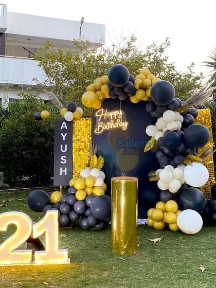 A stylish 21st birthday party in a garden with a black and gold theme, featuring a shimmer wall and marquee numbers.