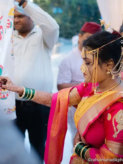 The bride performing a wedding ritual, her profile highlighting the traditional Maharashtrian jewelry and hairstyle.