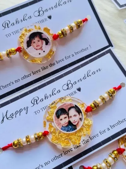 These beautiful rakhis feature a custom photo preserved in resin with gold flakes, presented on a "Happy Raksha Bandhan" card.