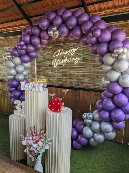 An outdoor 31st birthday party with a purple and silver balloon arch against a bamboo wall.