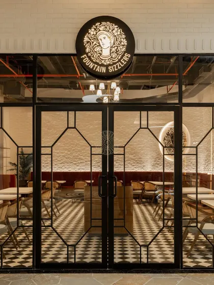 The view from the mall corridor into the restaurant, showcasing the inviting warmth of the interior through the elegant glass and metal facade.