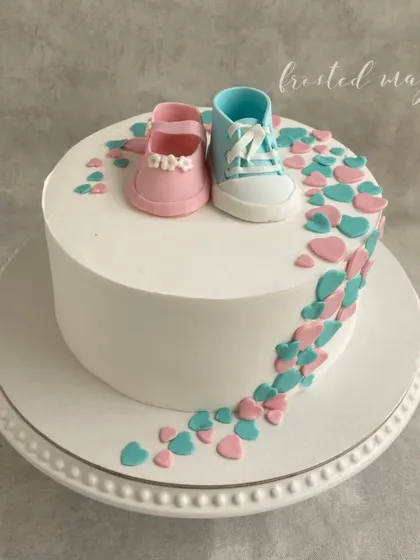 A sweet and simple cake for a baby shower. The handmade baby booties, one pink and one blue, are the centerpiece of this gender reveal or guessing game theme, with a cascade of tiny hearts.