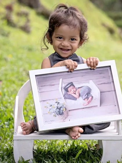 A proud little boy holding a framed photo from his own newborn session. This "then and now" shot, taken outdoors, is a beautiful way to document how much he has grown.
