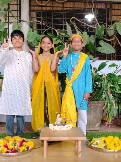 Three students in festive dress for Janmashtami, smiling and celebrating together. These events foster friendships and a strong sense of belonging.