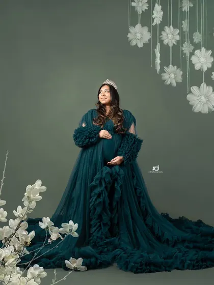 A regal portrait of a mom-to-be wearing a crown. The dramatic green gown and floral accents create a look that is both powerful and beautiful.