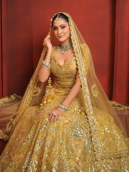 A full-length shot of the bride seated like royalty. The golden tones of her outfit and makeup create a look of pure elegance and grandeur.