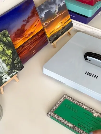 A corner of my desk showing some of my finished paintings, my gouache set, and other art supplies.