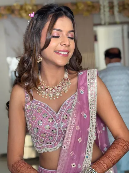 A close-up on the soft makeup and the gentle waves of the hair. A small flower is tucked into the side for a delicate touch.