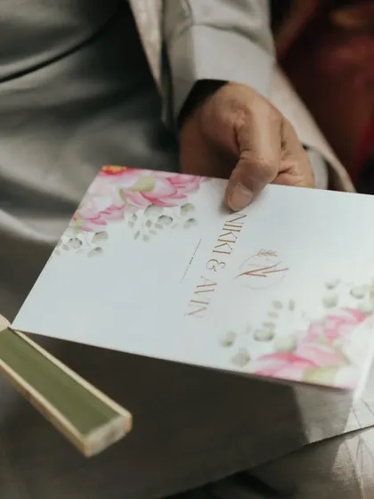 A guest holds the beautifully designed wedding program for Nikki & Avin, showing the elegant floral motif and custom monogram that was part of their wedding branding.