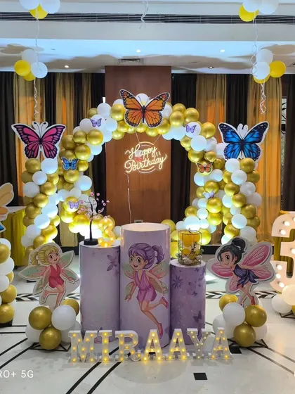 A full view of the fairy and butterfly theme in a party hall. The setup includes a circular balloon arch, themed pedestals, a light-up number '3', and marquee letters for the name.