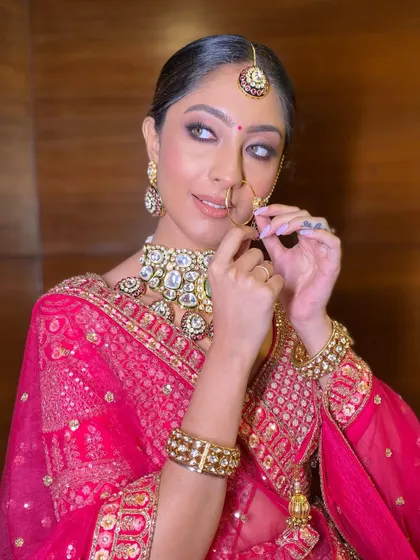A playful and chic pose. The close-up shows the sharp, defined eye makeup and the flawless base that stands up to the bold, traditional jewelry.