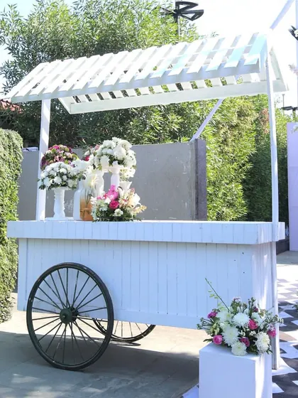 A classic white cart adorned with flowers, serving as a beautiful and functional decor piece within the carnival space.