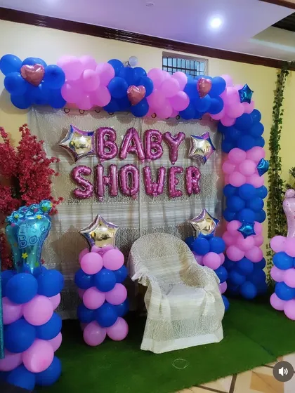 A baby shower decoration with a dedicated seat for the mother-to-be. The pink and blue balloon arch is accented with star and heart-shaped foil balloons.