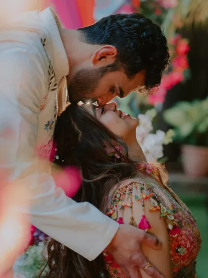 A tender forehead kiss during the Haldi ceremony. The bright, colorful background contrasts beautifully with this soft, intimate moment between the couple.