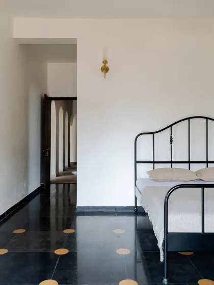The flooring in Maison Rouge combines polished black stone with traditional yellow inlay, a detail that pays homage to vernacular design. The simple iron bed frame provides a modern contrast, creating a balanced and eclectic aesthetic.