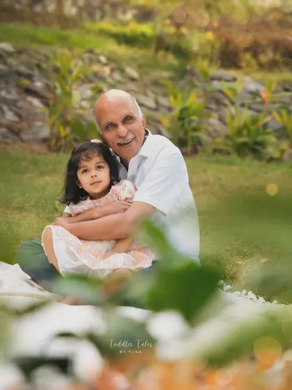 A grandfather shares a gentle hug with his granddaughter in a beautiful park setting. These portraits are treasured keepsakes of the special bond between generations.