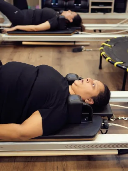 Lying on the Reformer, these clients are preparing for a series of abdominal exercises. The head and shoulder support ensures comfort while they focus on engaging their core.