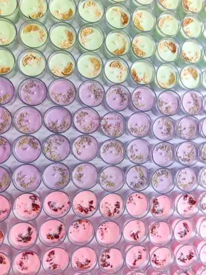 A Rainbow of Possibilities. This is what a large custom order looks like before it heads out. Rows of colorful votive candles, each topped with unique botanicals like dried lime, lavender, and rose petals, show the scale and variety I can offer for your brand or big event.