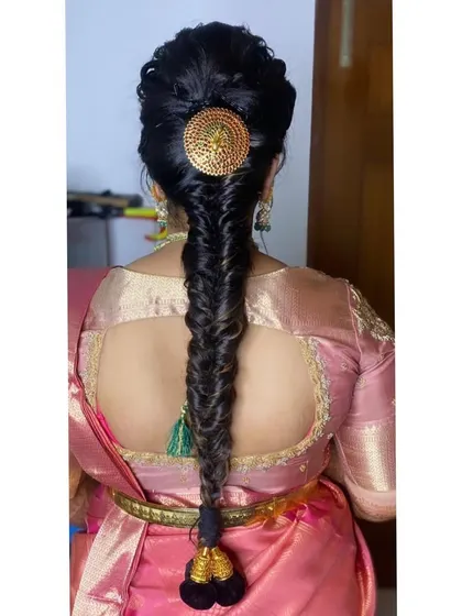A neat and elegant fishtail braid. This hairstyle is accented with a large, round gold-plated hair pin, giving it a touch of traditional grandeur.