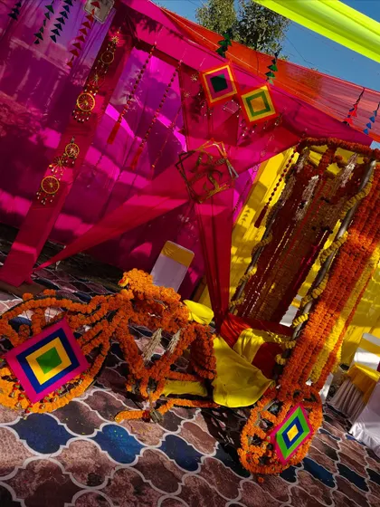 A close-up of the vibrant decor elements from a traditional Haldi. The bright pink and yellow fabrics are complemented by handmade tassels and marigold decorations.