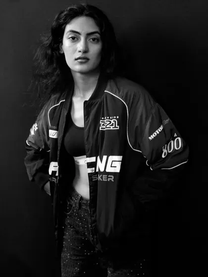 A strong and confident black and white portrait. The high-contrast lighting and dark background create a moody, editorial feel, highlighting the model's powerful presence.