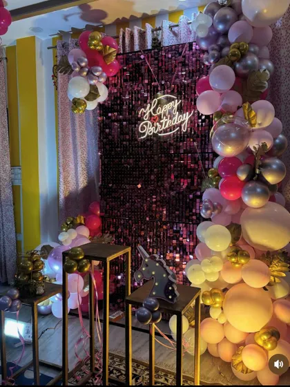 This chic birthday decoration combines a shimmer wall, a neon sign, and an elaborate balloon garland for a very glamorous party look.